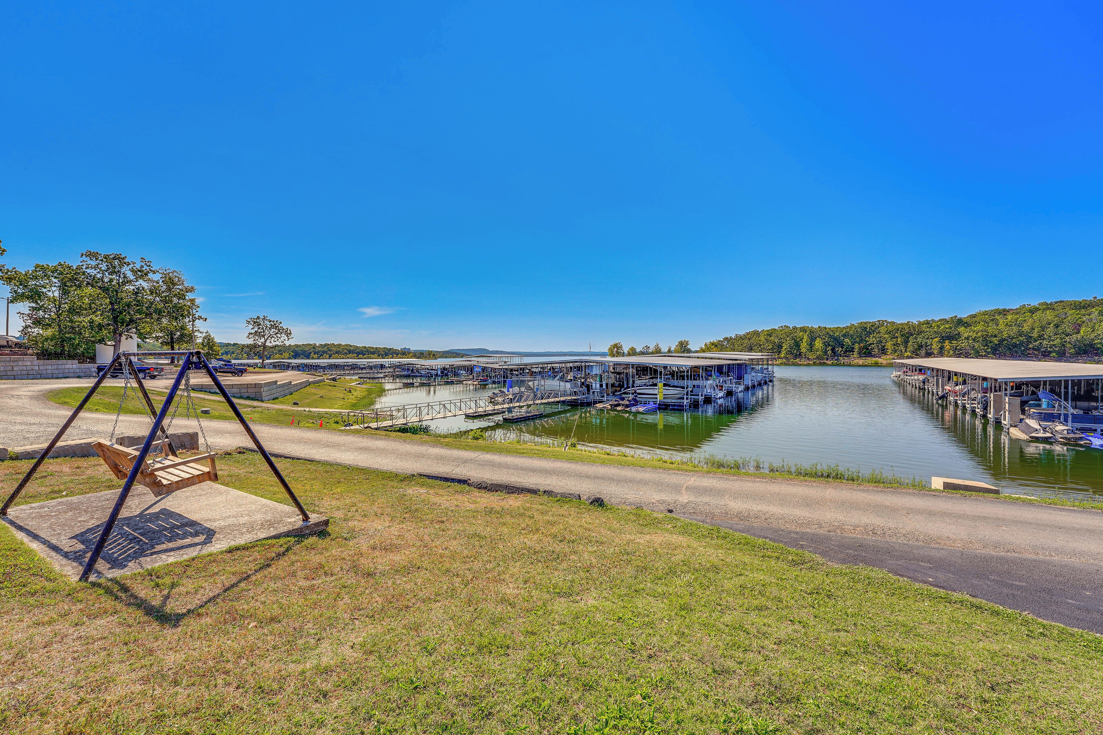 A riverside view with a swing set, a dock with boats, and a covered area with a roof.
