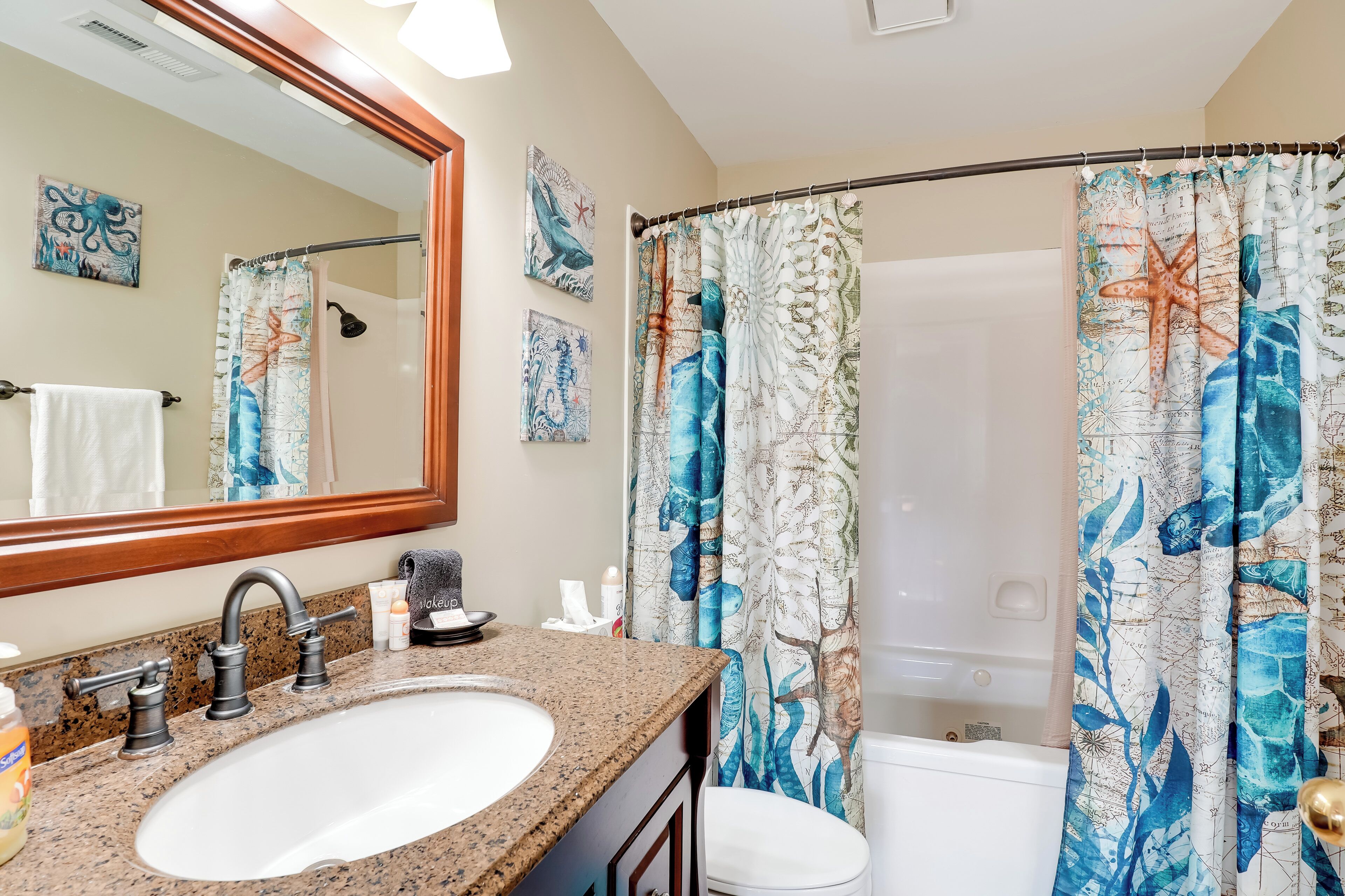 Une salle de bain avec un lavabo sur un plan de travail en granit, un miroir et un rideau de douche à motifs nautiques.