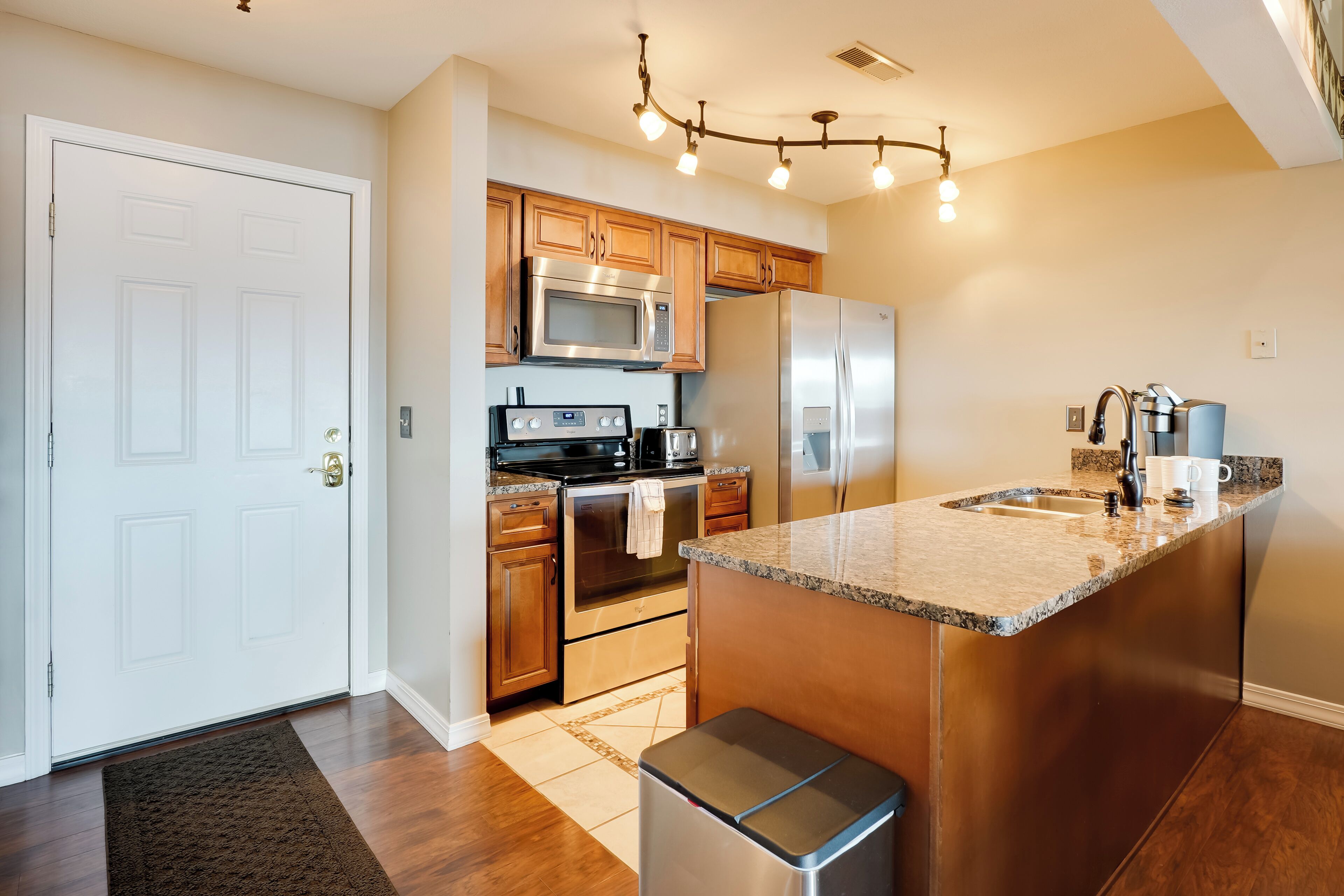 A modern kitchen with wooden cabinets, stainless steel appliances, a granite countertop, and a built-in island with a sink.