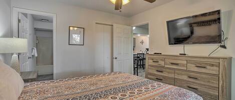 A bedroom with a patterned bedspread, a ceiling fan, a TV mounted on the wall, and a wooden dresser.