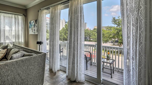 A balcony with a view of trees and buildings, a sofa, and a table with a vase and a bottle. - 1 Block to Beach! Breezy Myrtle Beach Getaway (Myrtle Beach)