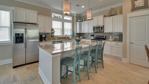 A modern kitchen with white cabinets, a stainless steel refrigerator, a large island with bar stools, and a microwave. - 1 Block to Beach! Breezy Myrtle Beach Getaway (Myrtle Beach)