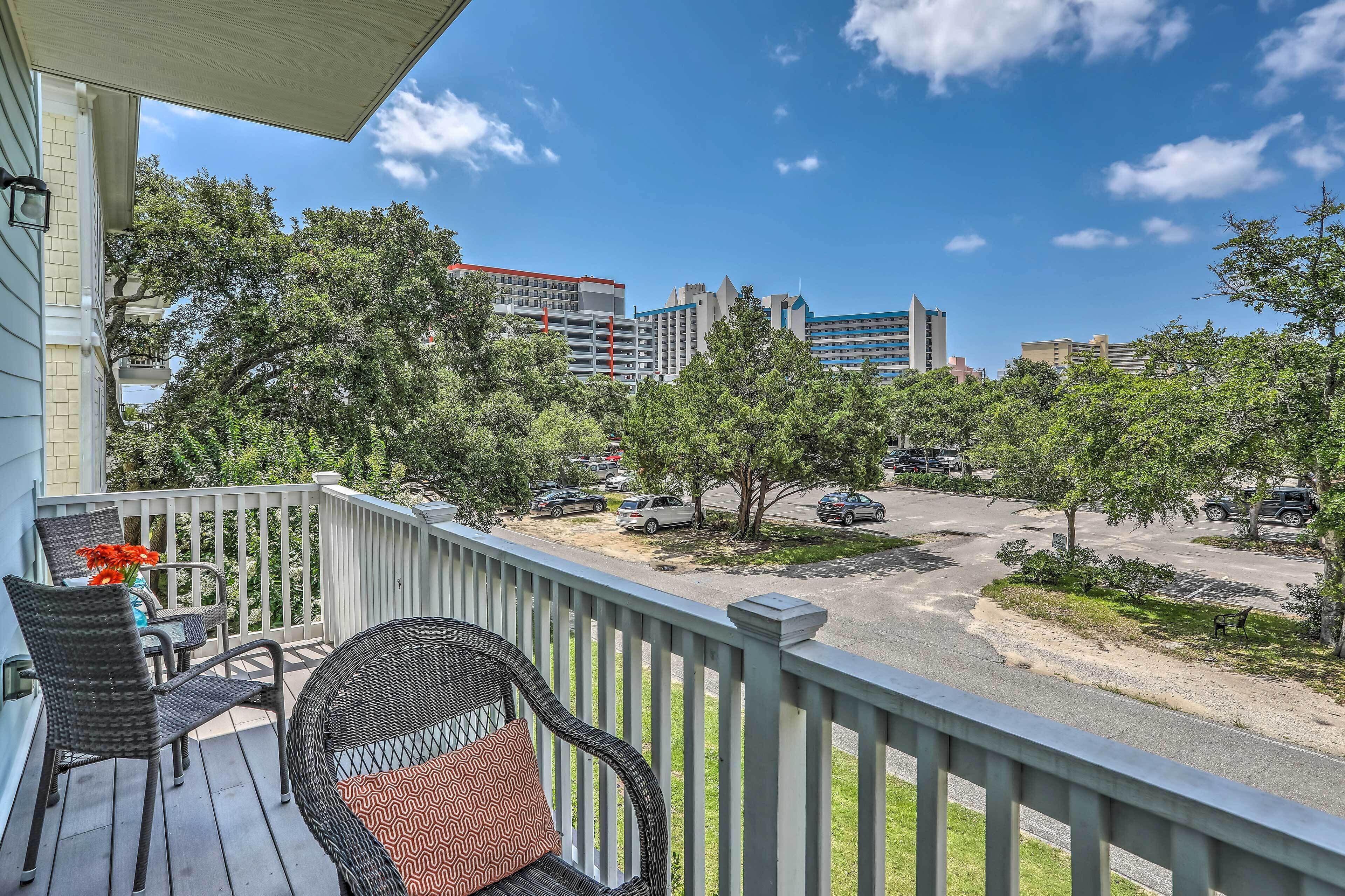 A balcony with wicker furniture and a view of a parking lot and buildings.