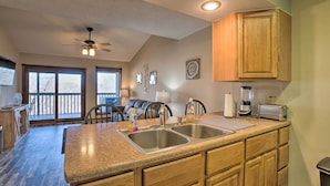 A kitchen with a granite countertop, stainless steel sink, wooden cabinets, a ceiling fan, and a view to a balcony. - Branson West Condo Rental w/ Pool Access! (Branson West)