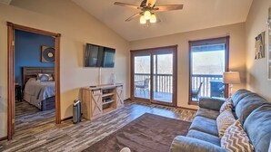 A spacious living room with a ceiling fan, a large window, a sofa, and a wooden entertainment center. - Branson West Condo Rental w/ Pool Access! (Branson West)