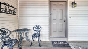 A porch with a welcome sign, two chairs, a small table, a door, and a lantern.