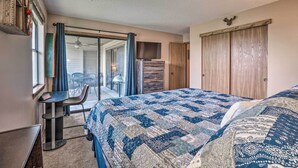 A bedroom with a large bed, a desk, and a chair. There is a sliding glass door leading to a balcony.