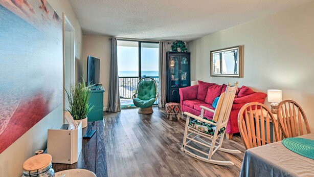A living room with a view of the ocean, a red sofa, a rocking chair, and a dining area with a table. - Bright Myrtle Beach Condo w/ Private Balcony! (Myrtle Beach)