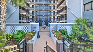 A multi-story residential building with balconies, a central courtyard with a fountain, and landscaped areas with plants and flowers. - Bright Myrtle Beach Condo w/ Private Balcony! (Myrtle Beach)