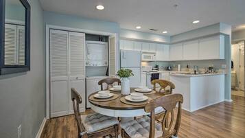 A modern kitchen with white cabinets, a wooden dining table with four chairs, and a built-in island with a sink.