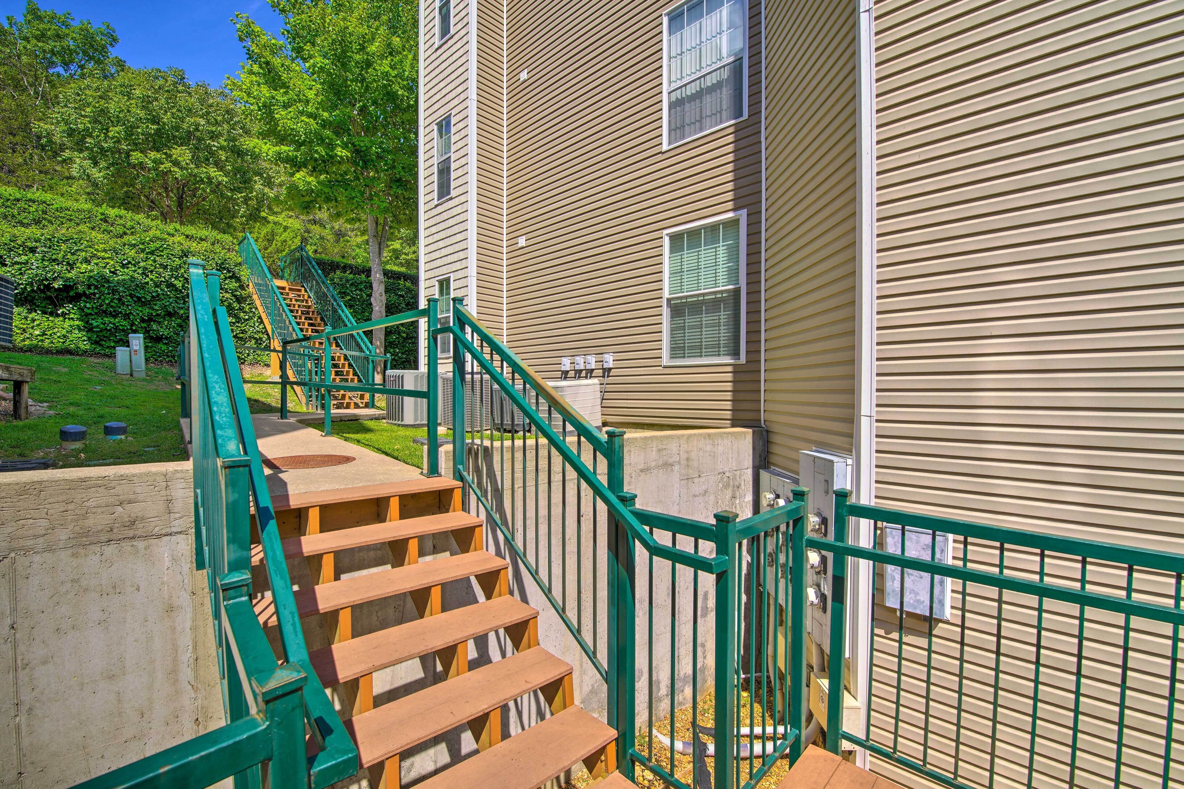 A wooden staircase with green railings leading to a building with beige siding.