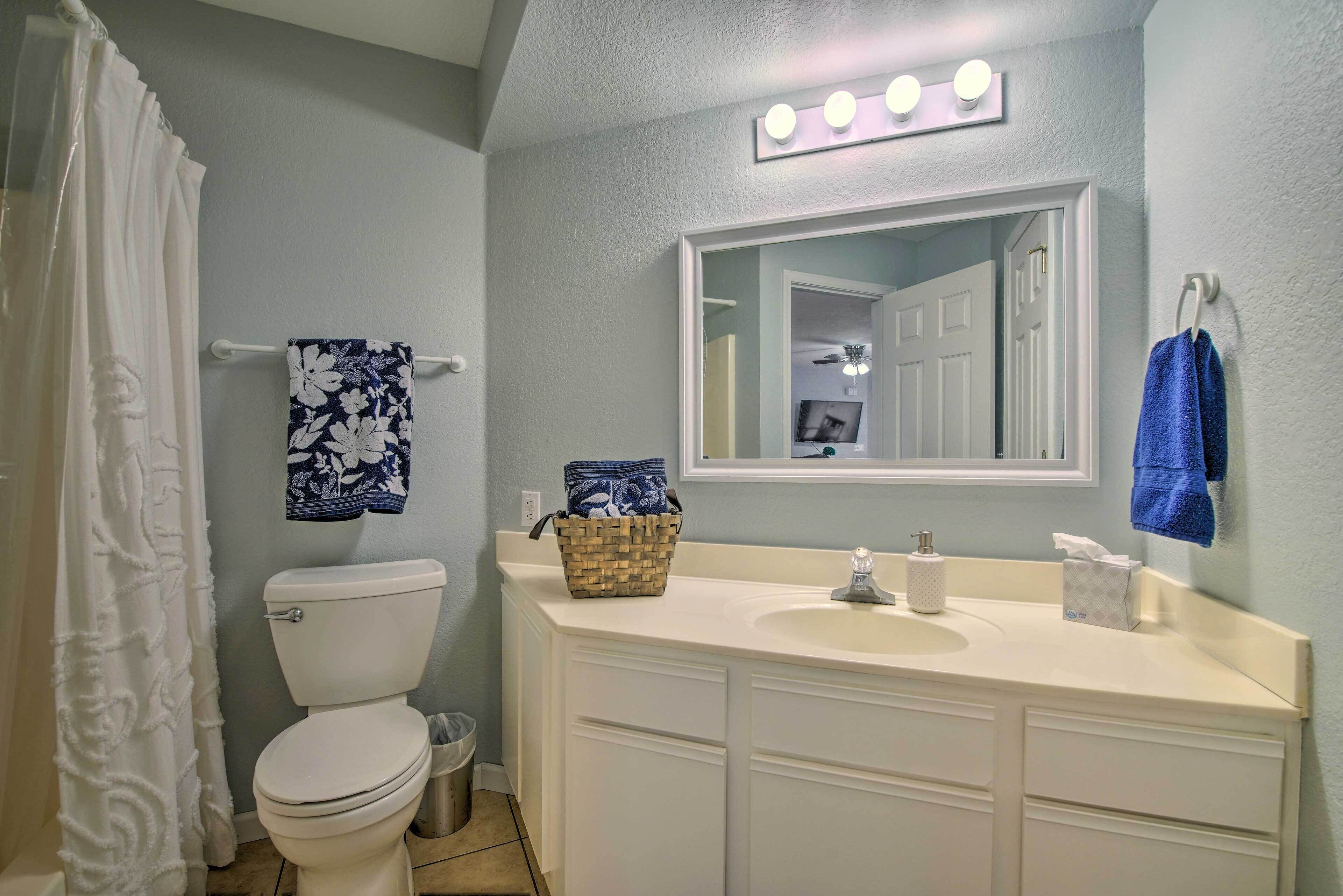 Une salle de bain avec des toilettes blanches, un lavabo avec un miroir au-dessus et un rideau de douche.