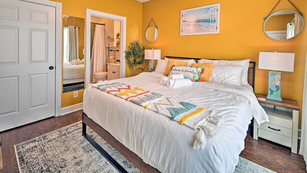 Un dormitorio con cama, mesitas de noche, un espejo y una puerta que da a otra habitación.