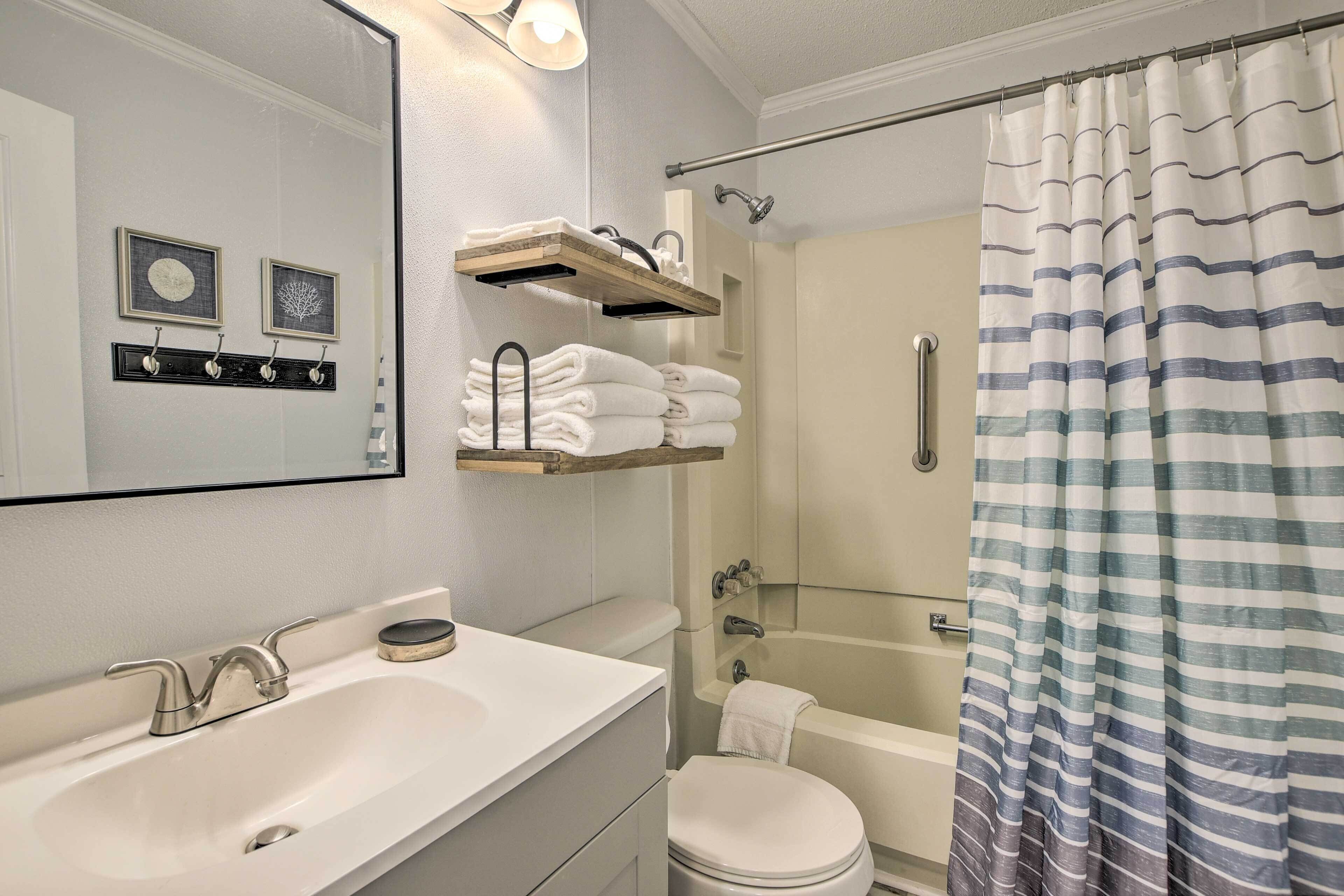 Une salle de bain avec un lavabo blanc, des toilettes et un espace douche. On y trouve des porte-serviettes et des étagères au-dessus du lavabo.