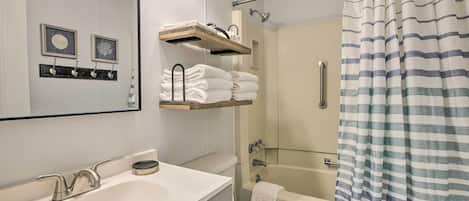 Une salle de bain avec un lavabo blanc, des toilettes et un espace douche. On y trouve des porte-serviettes et des étagères au-dessus du lavabo.