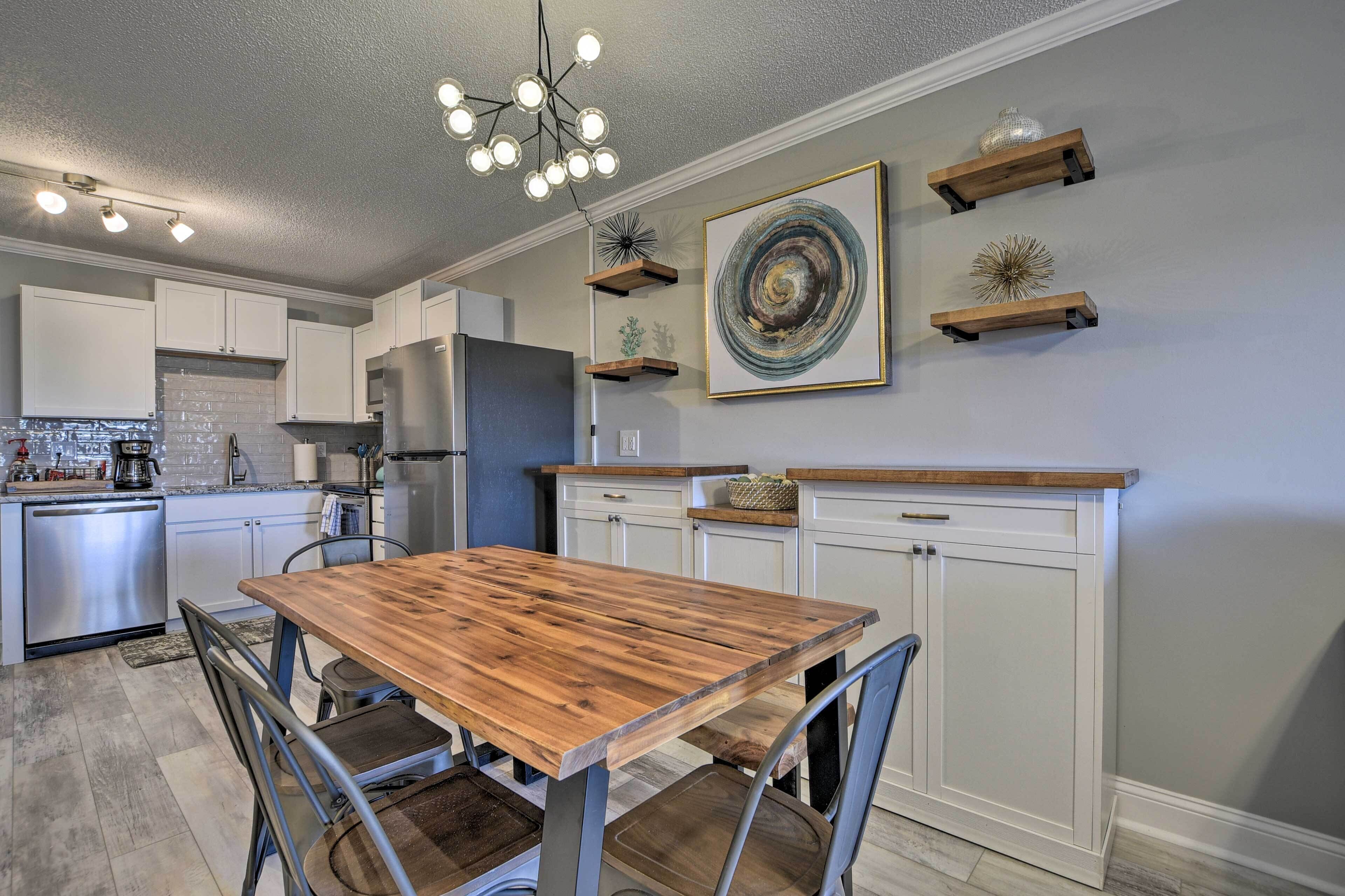 A modern kitchen with white cabinetry, a wooden dining table, and a chandelier.