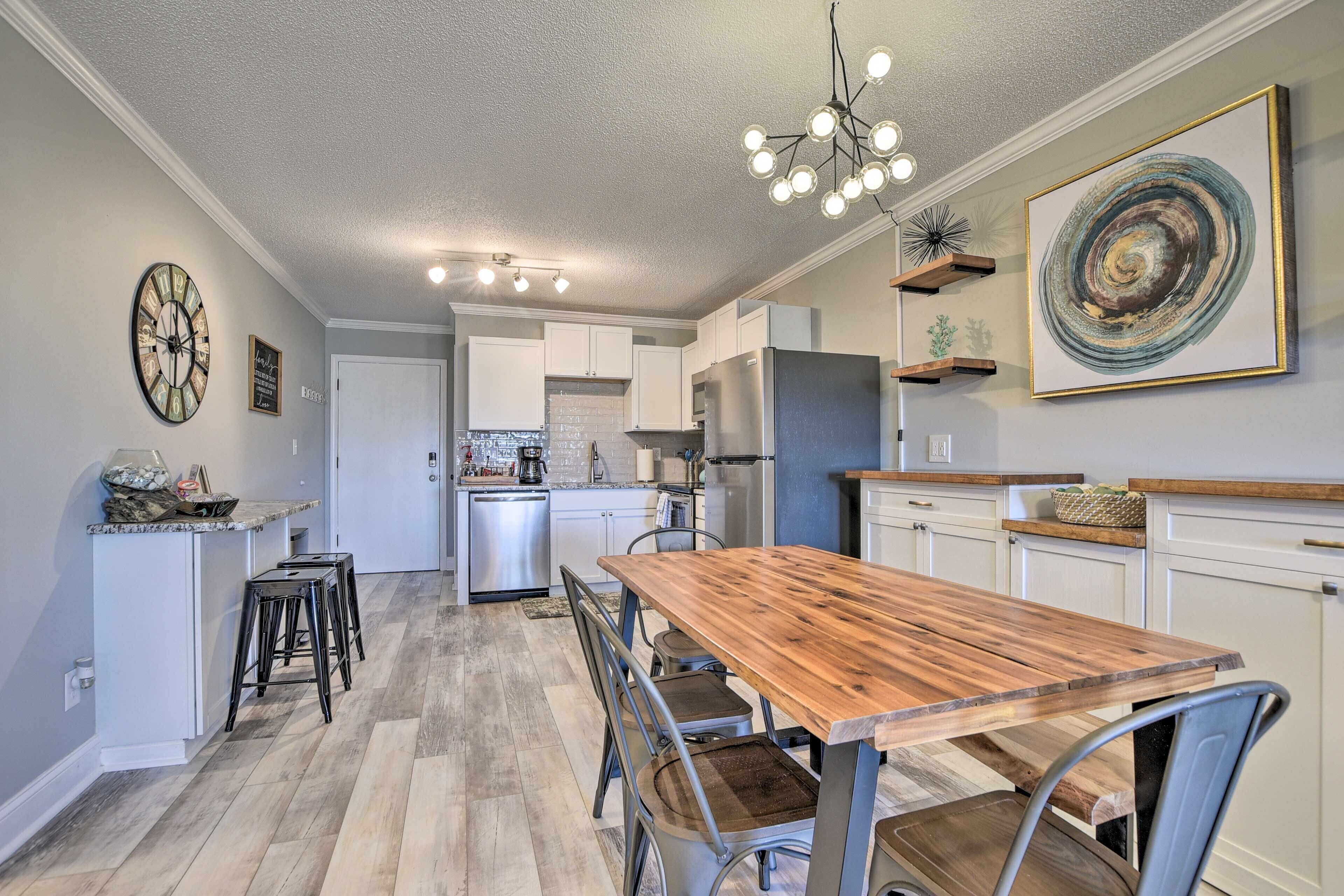 A kitchen with a wooden dining table, bar stools, a chandelier, and a large abstract painting.