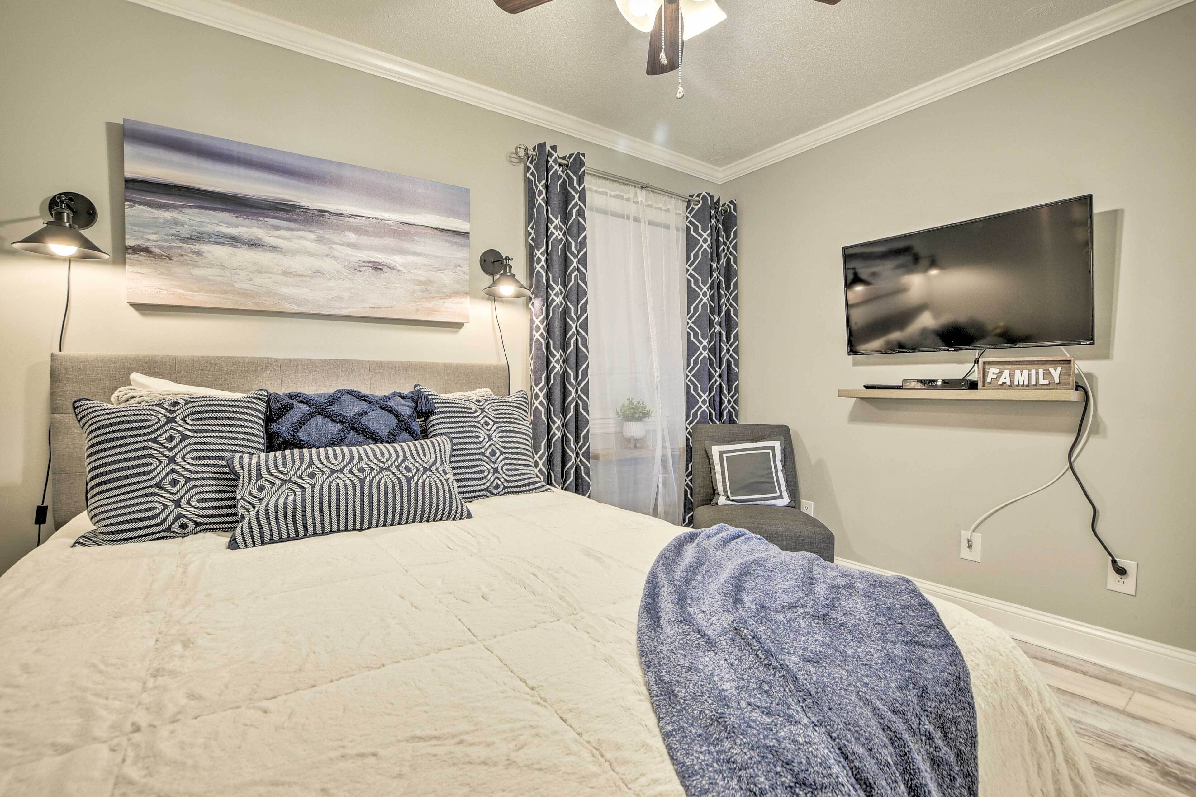 A bedroom with a bed, a TV, a ceiling fan, and a painting on the wall.