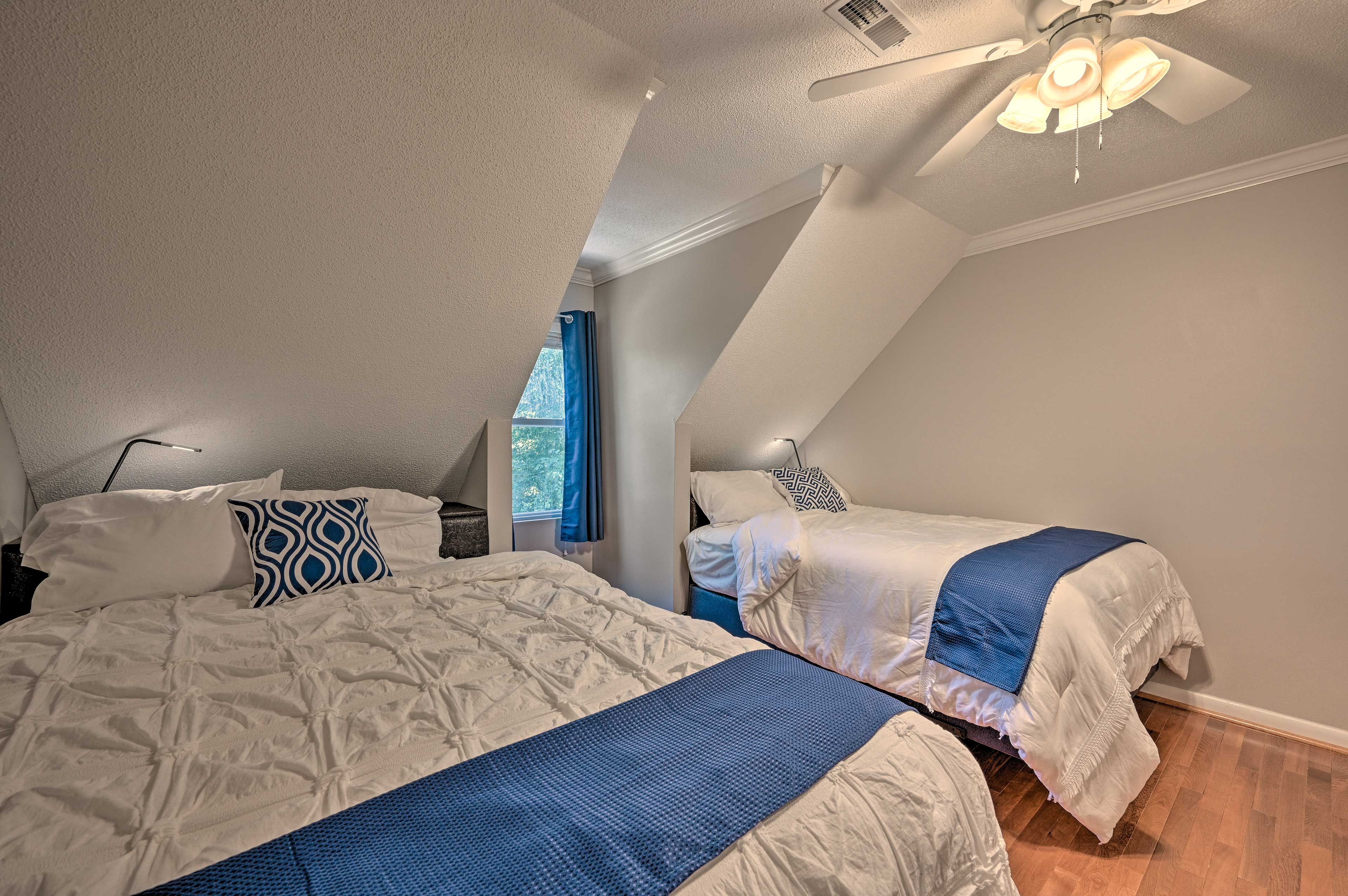 A bedroom with two beds, a ceiling fan, and a window with blue curtains.