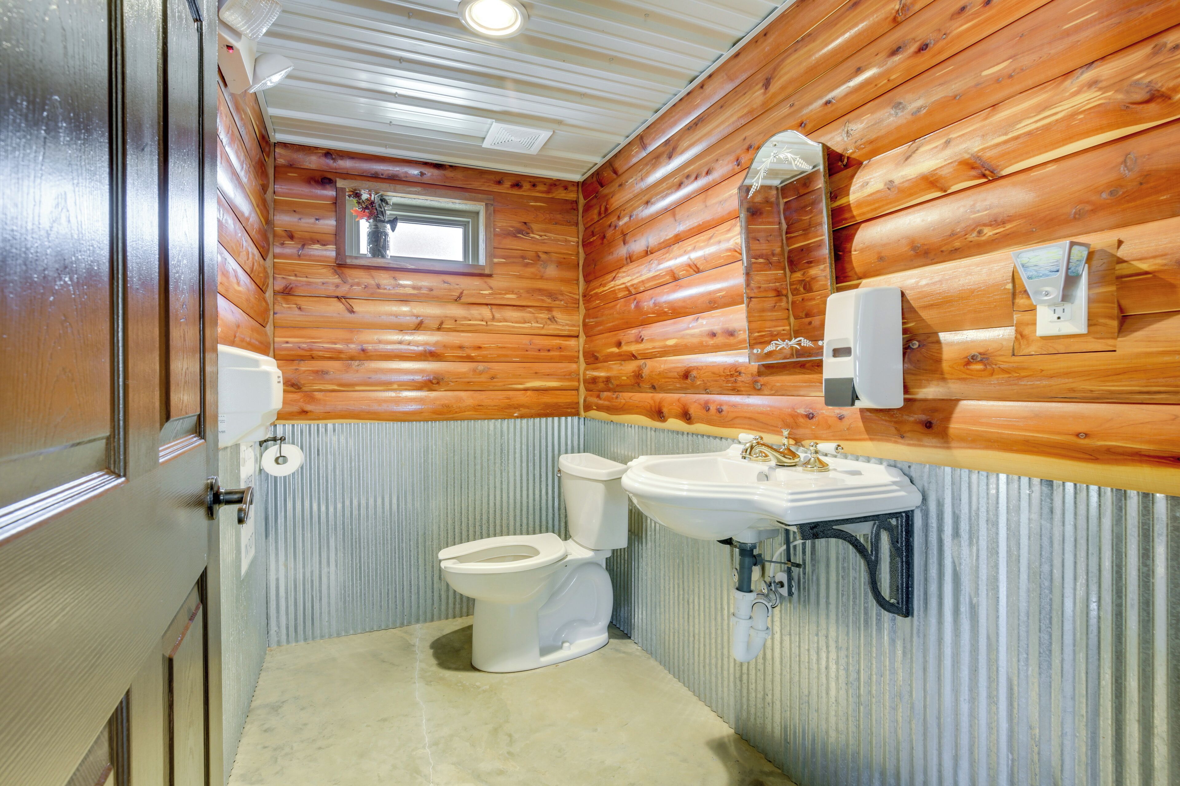 A bathroom with wooden walls, a toilet, a sink, and a window.