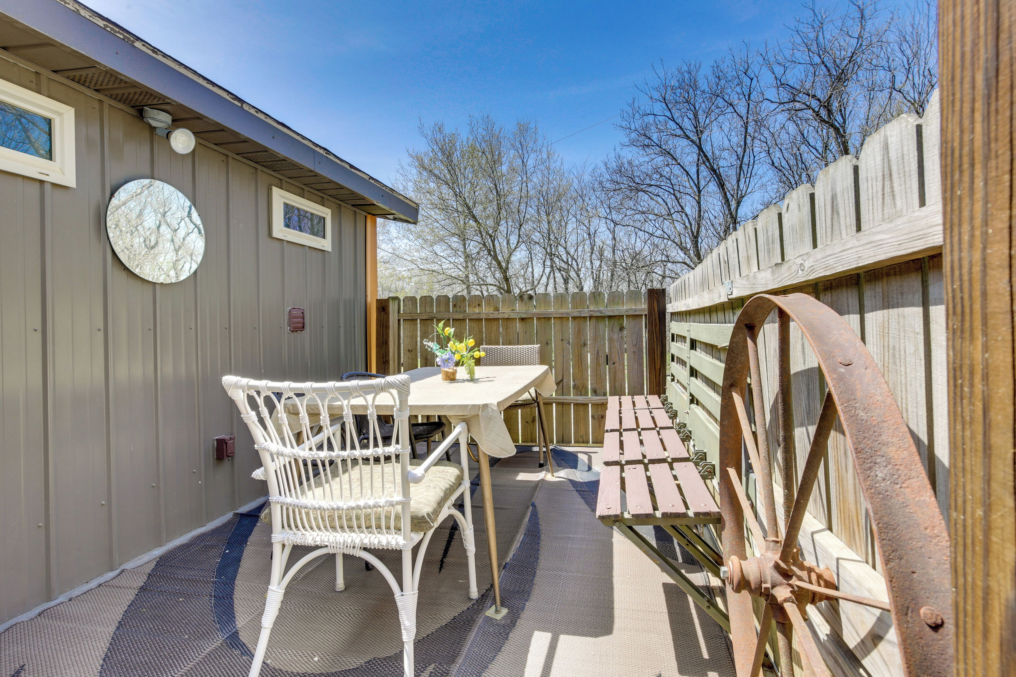 A patio with a table and chairs, a wooden fence, and a large wheel.