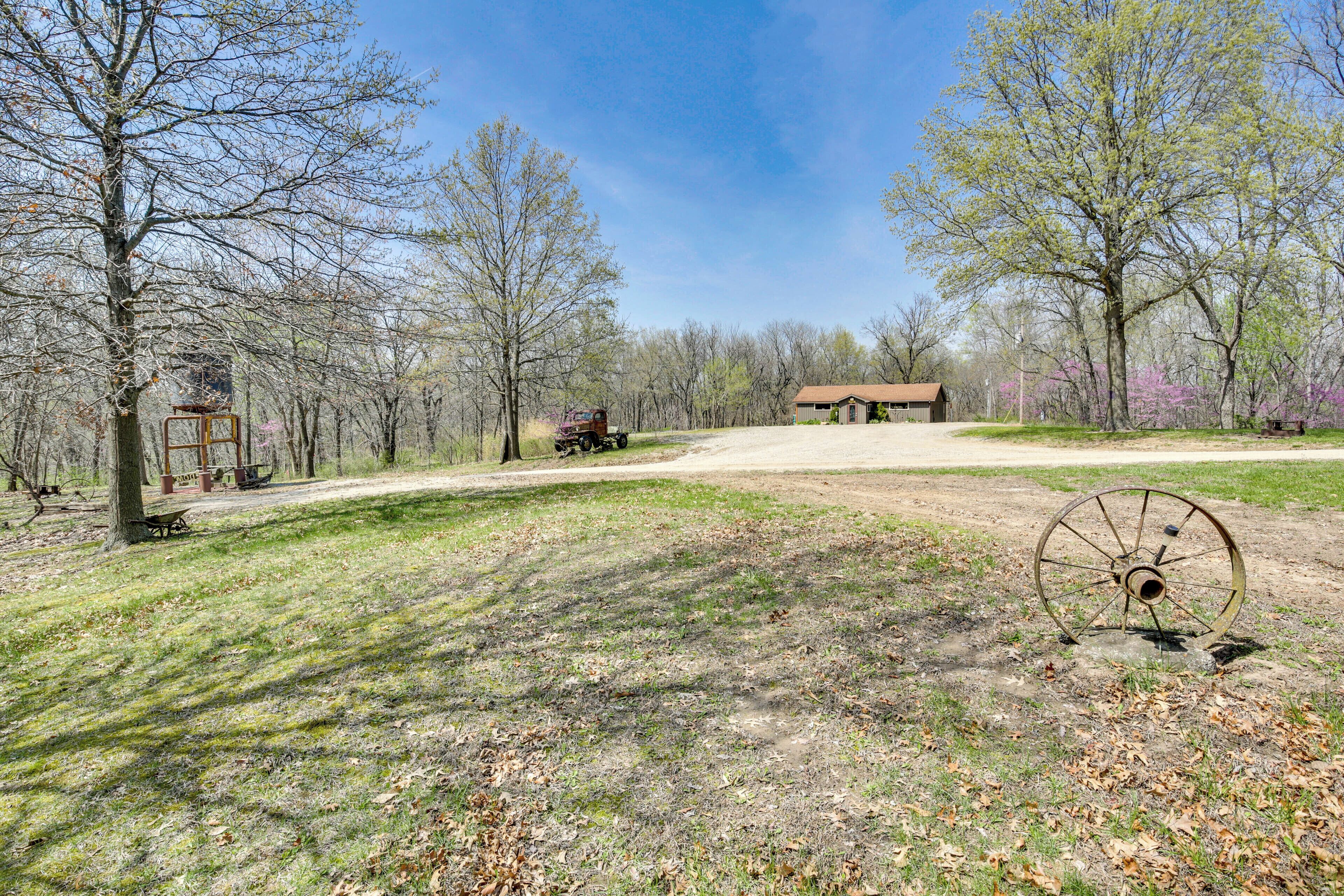 A rural landscape with a dirt path, a large metal wheel, and a wooden structure in the distance.