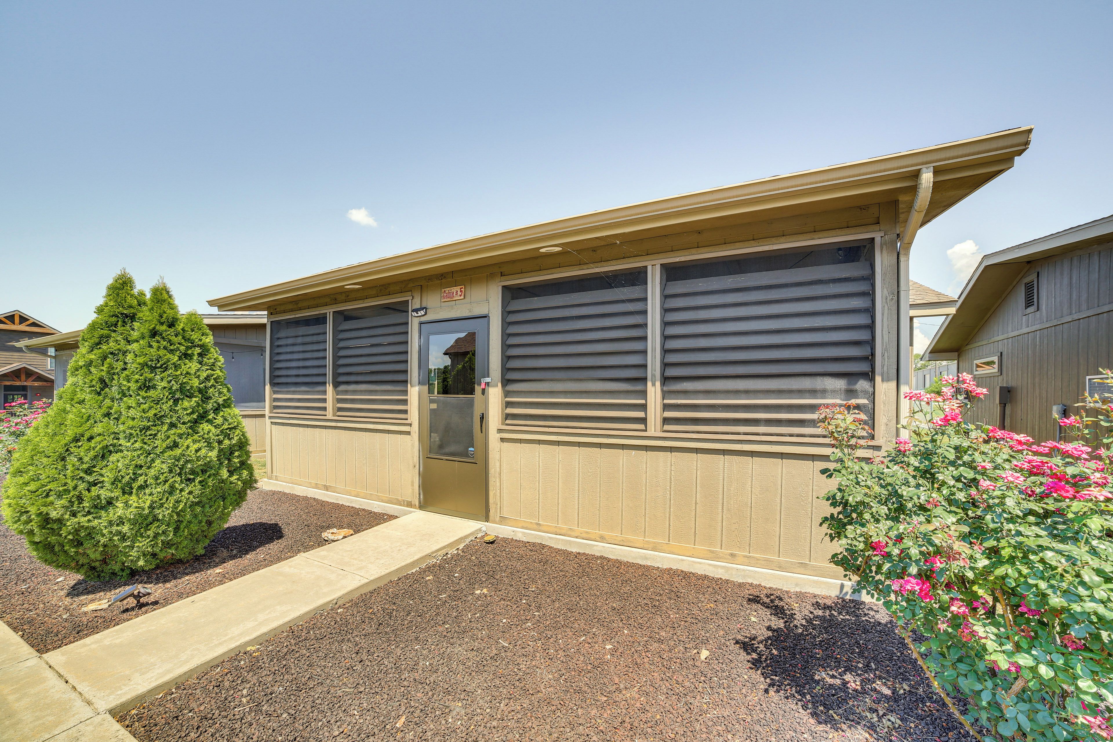 A building with a garage door, a small tree, and a flower bush.