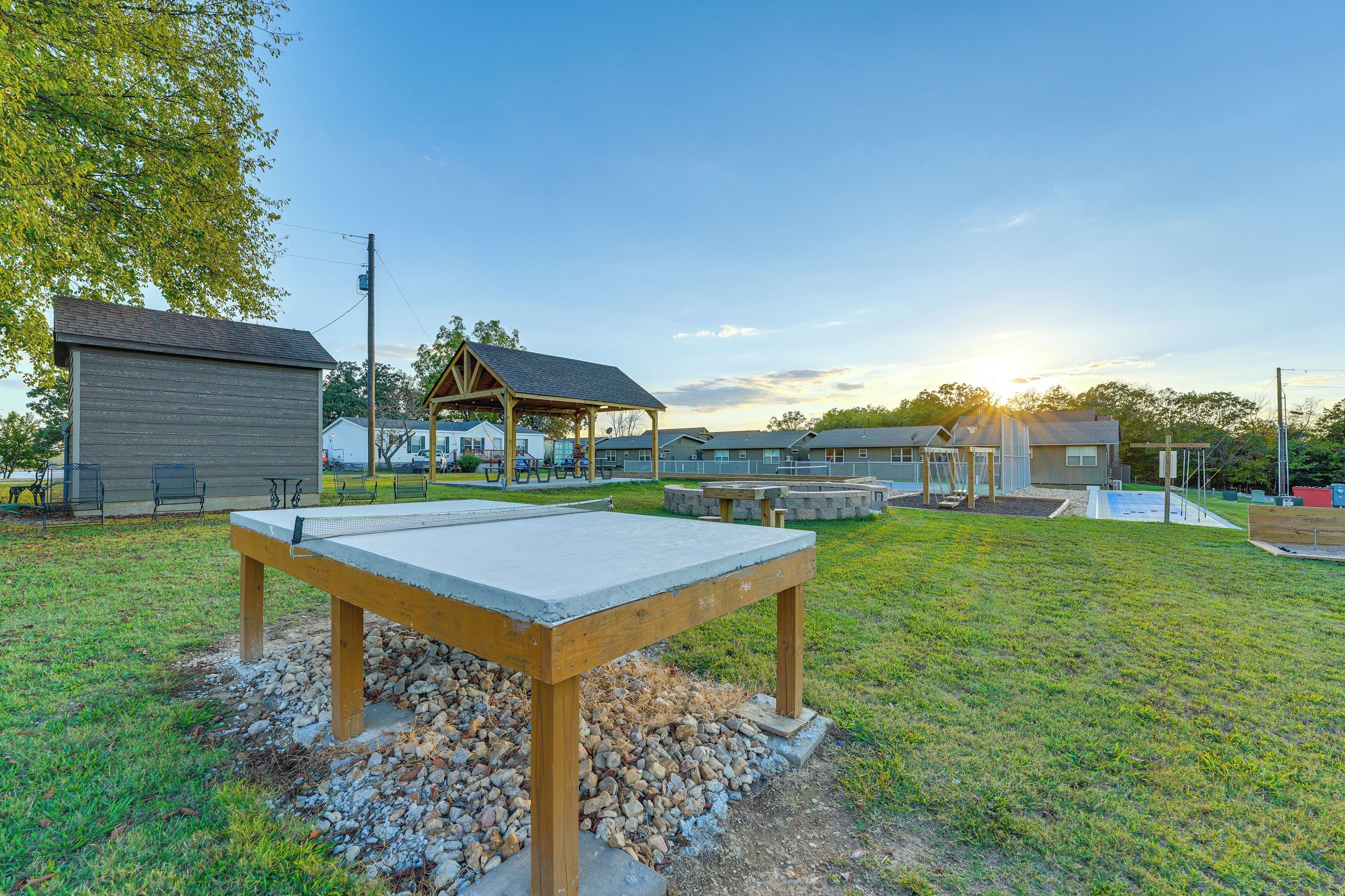 Une table en béton avec des pieds en bois, située dans un espace verdoyant, avec un belvédère et un bâtiment en arrière-plan.