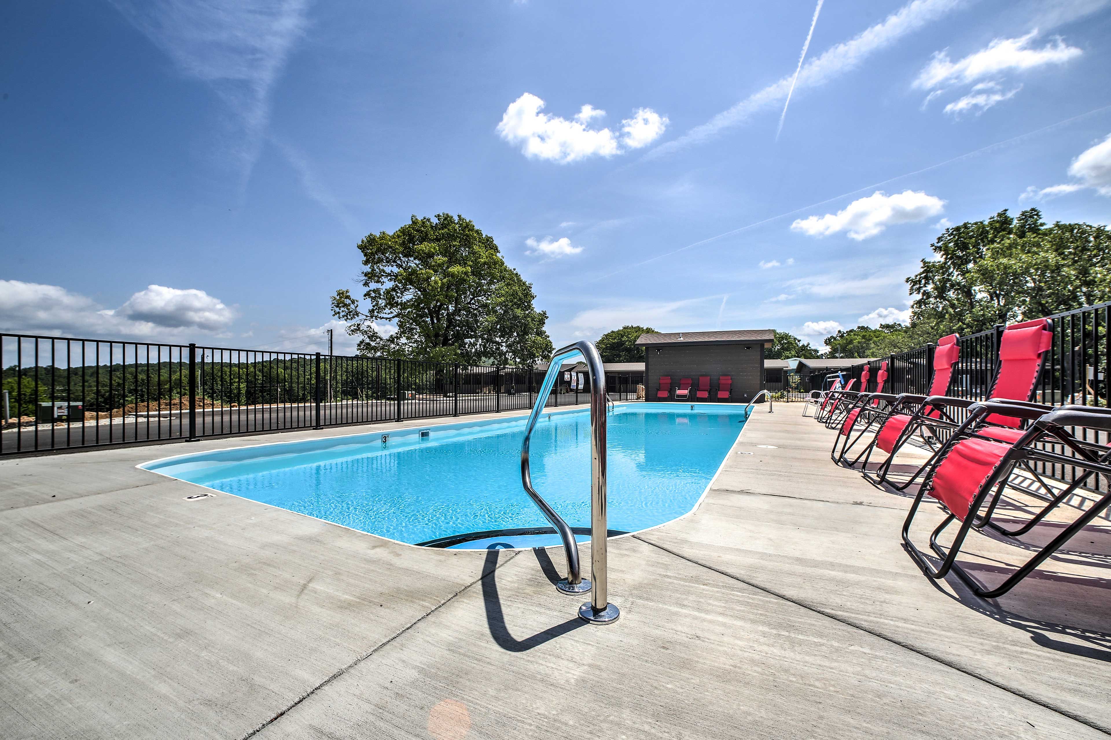A swimming pool with a metal ladder, red chairs, and a fenced area.