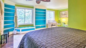 A bedroom with a large bed, built-in shelving, a ceiling fan, and a window with a view of trees. - Cheery Swansea Home on Calmont Pond w/ Dock! (Swansea)