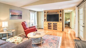 A living room with a red chair, a round coffee table, a flat-screen TV on a wooden entertainment unit, and a patterned rug. - Cheery Swansea Home on Calmont Pond w/ Dock! (Swansea)
