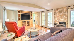 A living room with a red leather chair, a grey sofa, a flat-screen TV, and a stone fireplace. - Cheery Swansea Home on Calmont Pond w/ Dock! (Swansea)