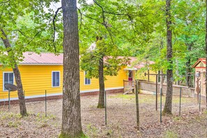 A yellow building with a red roof, surrounded by trees and a fenced area. - Cheery Swansea Home on Calmont Pond w/ Dock! (Swansea)