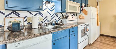 A modern kitchen with blue cabinets, a white dishwasher, a microwave, and a refrigerator.