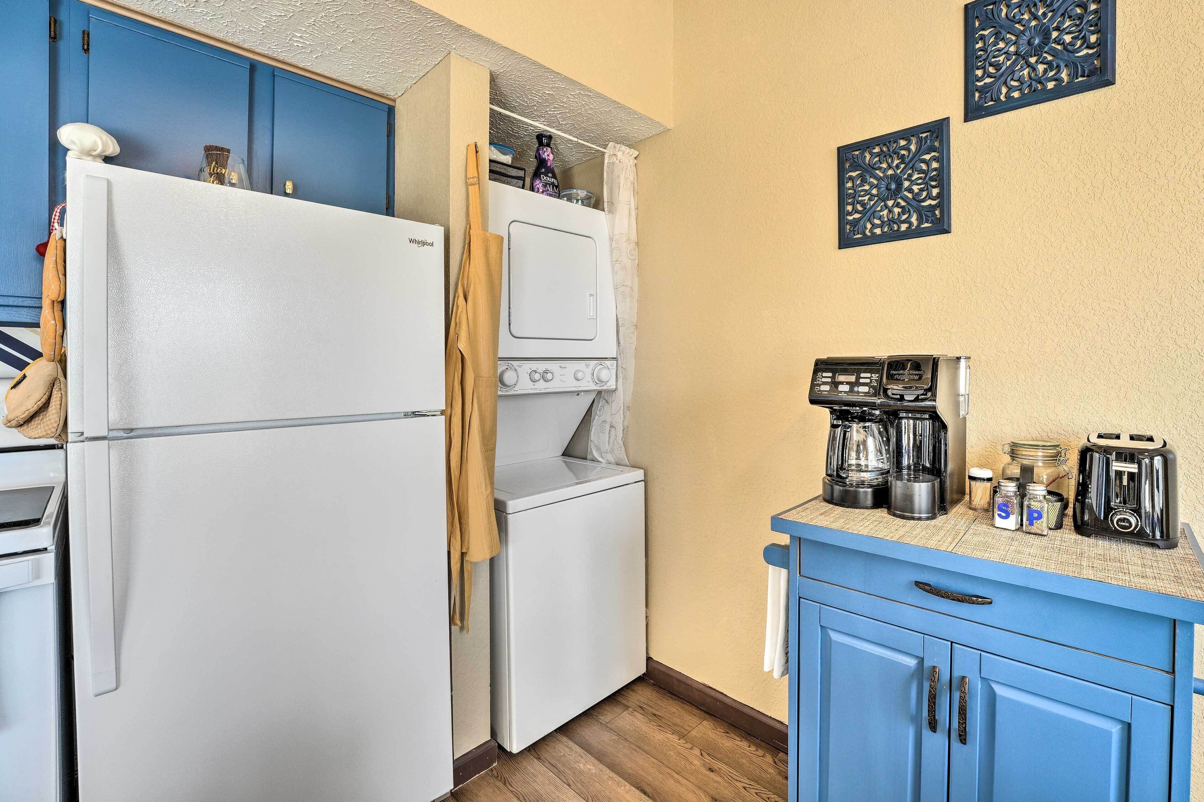 A compact kitchen with a white refrigerator, a washing machine, a coffee maker, and a toaster.