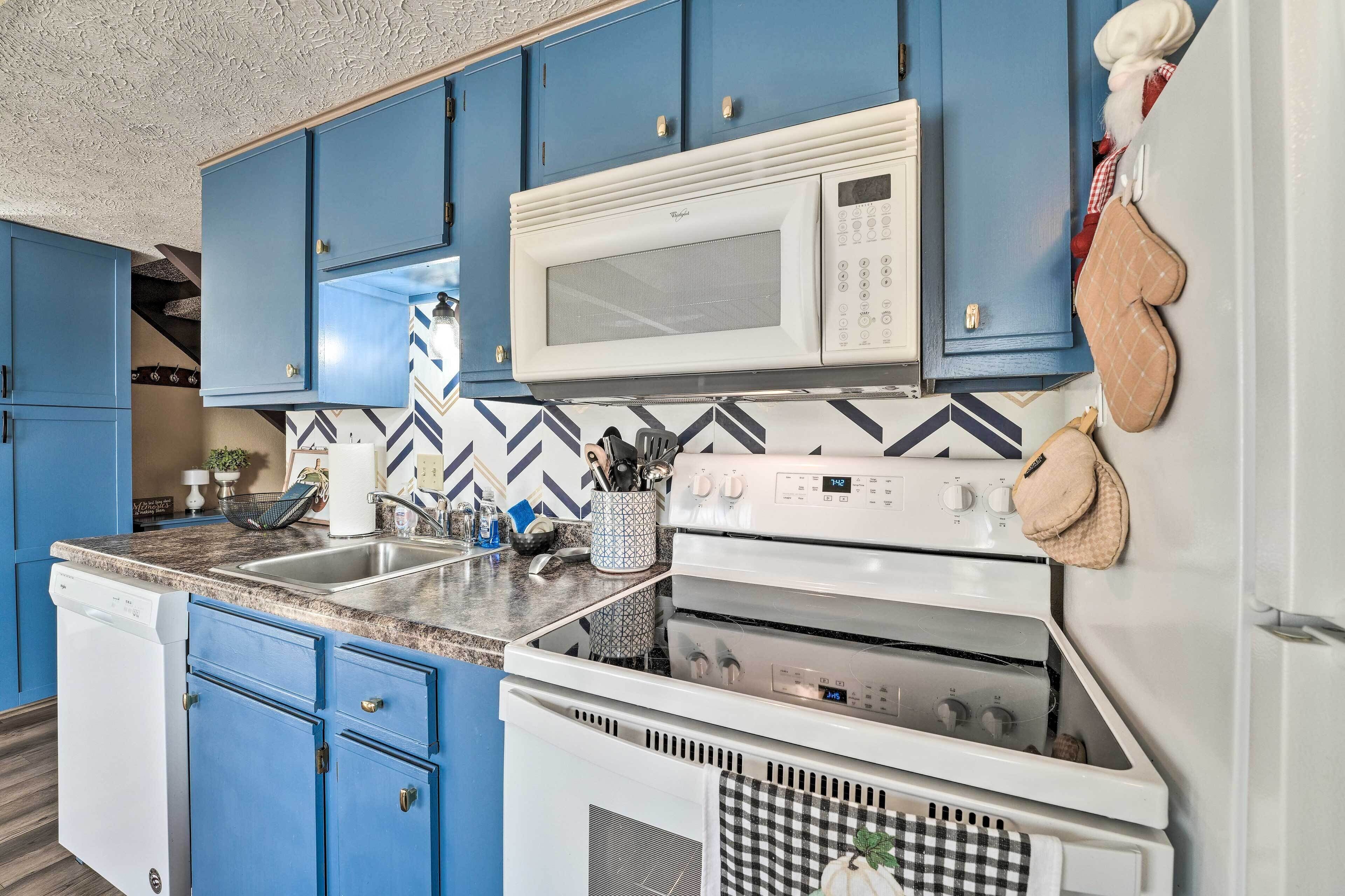 A kitchen with blue cabinets, a white microwave, a stove, and a dishwasher.