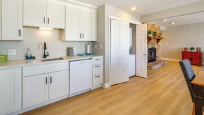 A modern kitchen with white cabinetry, a dishwasher, and a dining area with a wooden table and a red chair.