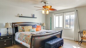 A bedroom with a bed, bedside tables, a ceiling fan, a window with curtains, and a chair.