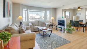 A modern living room with a sofa, coffee table, TV, and dining area.