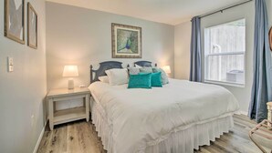 A neatly arranged bedroom with a bed, bedside lamps, a nightstand, a window with curtains, and a wall-mounted picture. - Cheerful Condo: Patio, 2 Mi to Branson Strip! (Branson)