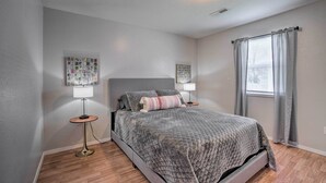 Une chambre à coucher comprenant un lit, deux tables de chevet, une lampe, un tableau décoratif et une fenêtre avec des rideaux.