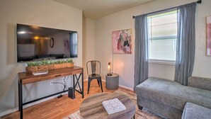 Un salon avec un meuble TV en bois, un canapé gris, une table basse ronde et une fenêtre avec des rideaux.