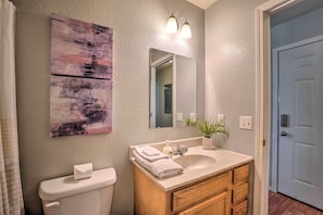 A bathroom with a toilet, sink, and mirror. There is a painting on the wall and a plant on the counter. - Charming One-level Home w/ Deck, Walk to Dtwn (West Plains)