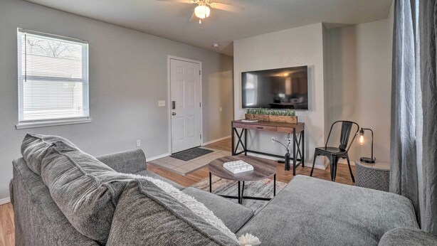 Un salon moderne avec un canapé gris, une table basse, un ventilateur de plafond, un téléviseur et un petit coin repas.