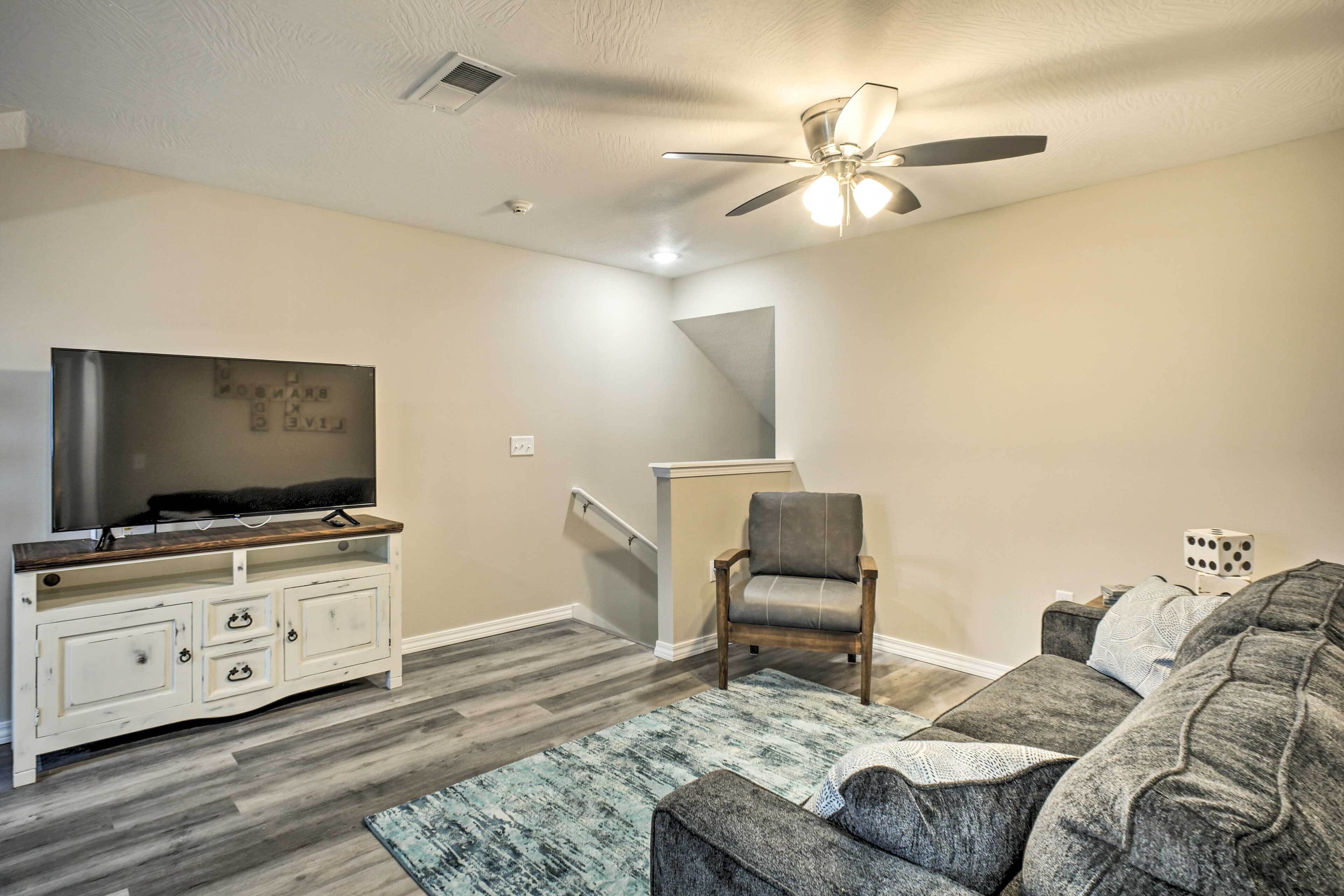 A living room with a TV on a white cabinet, a gray sofa, a wooden chair, and a blue rug.