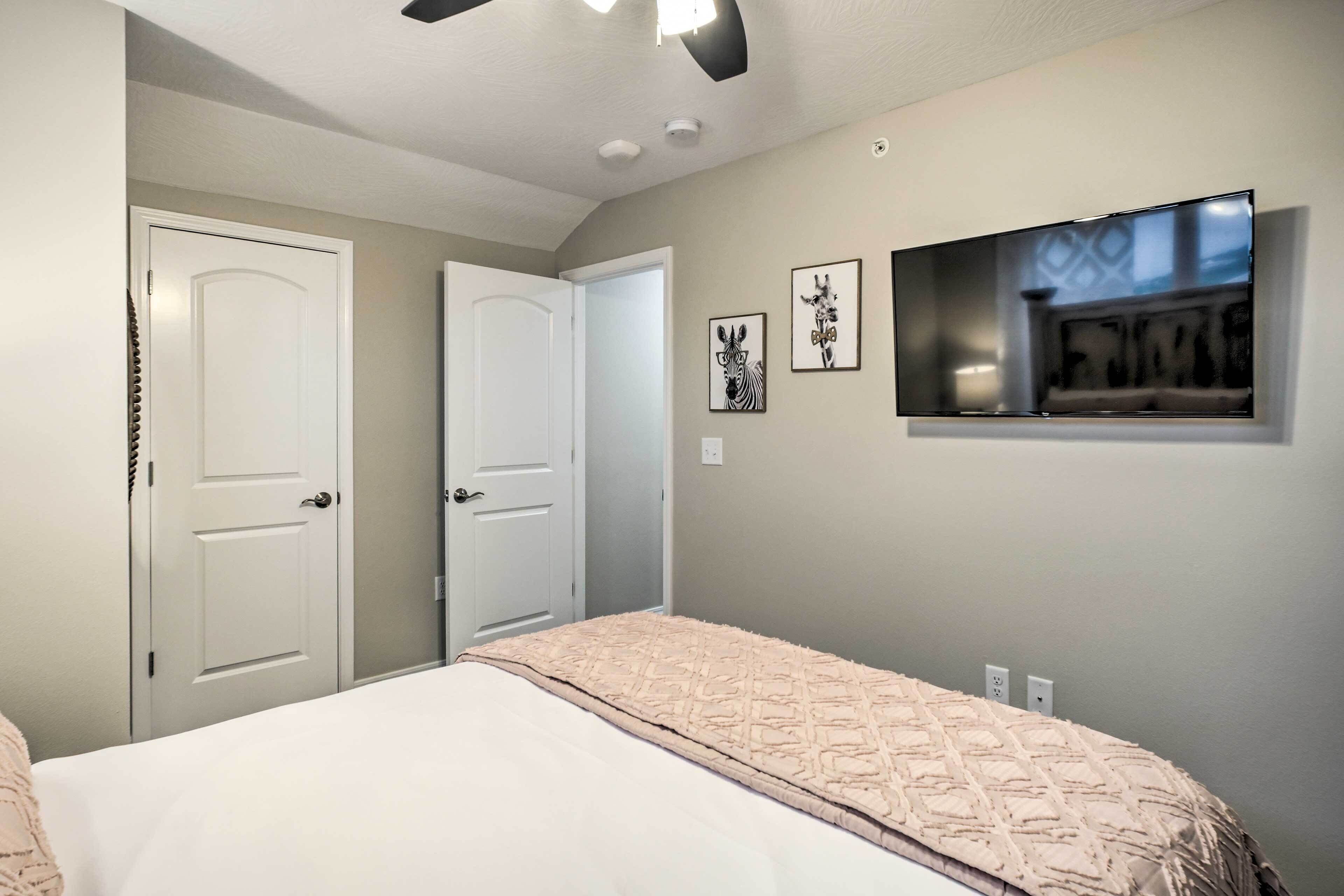 A bedroom with a bed, a ceiling fan, a TV mounted on the wall, and two doors.