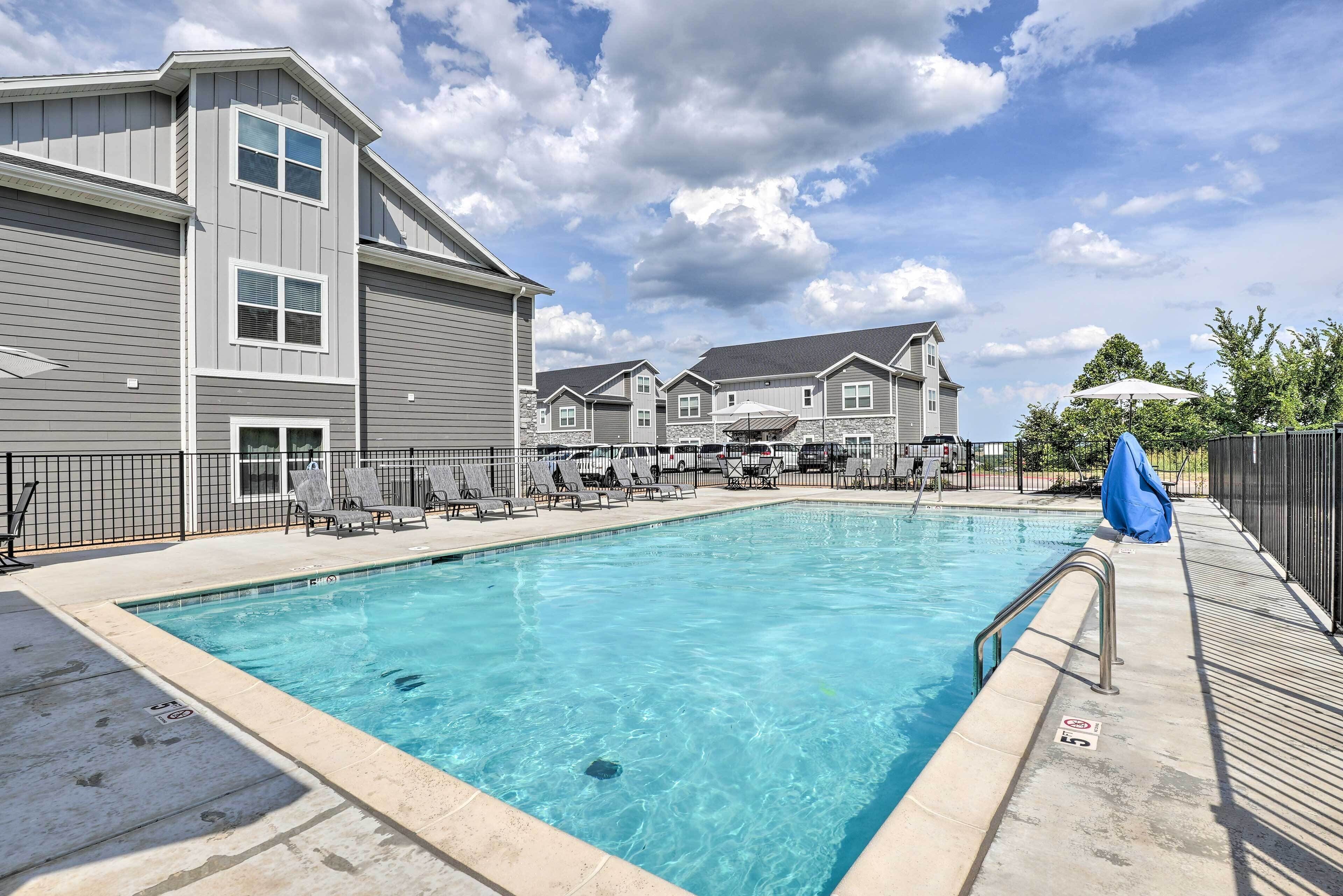 A swimming pool with lounge chairs and umbrellas, surrounded by multi-story buildings with a clear sky above.