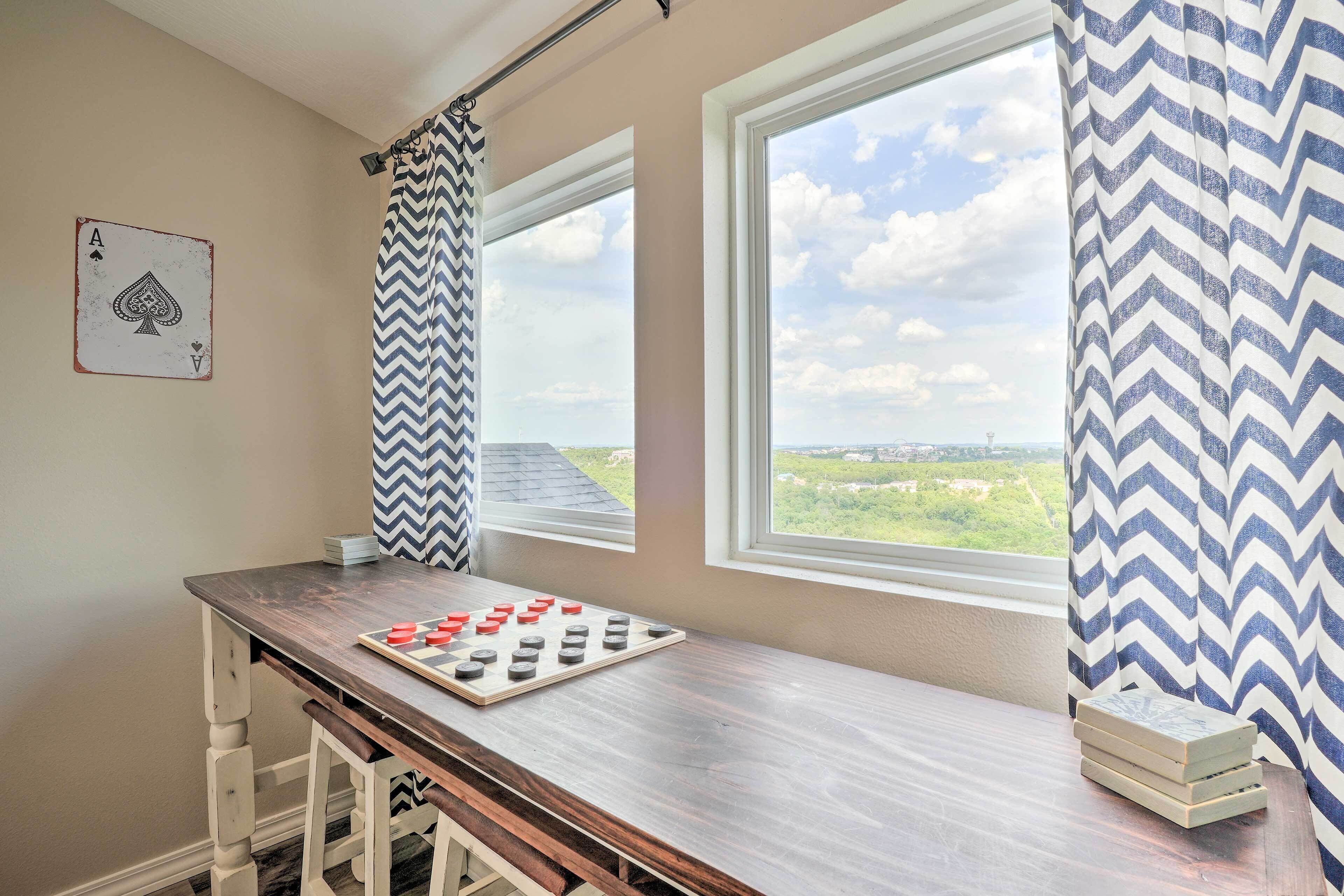 A room with a wooden table, a chessboard, and a window with a view of greenery.