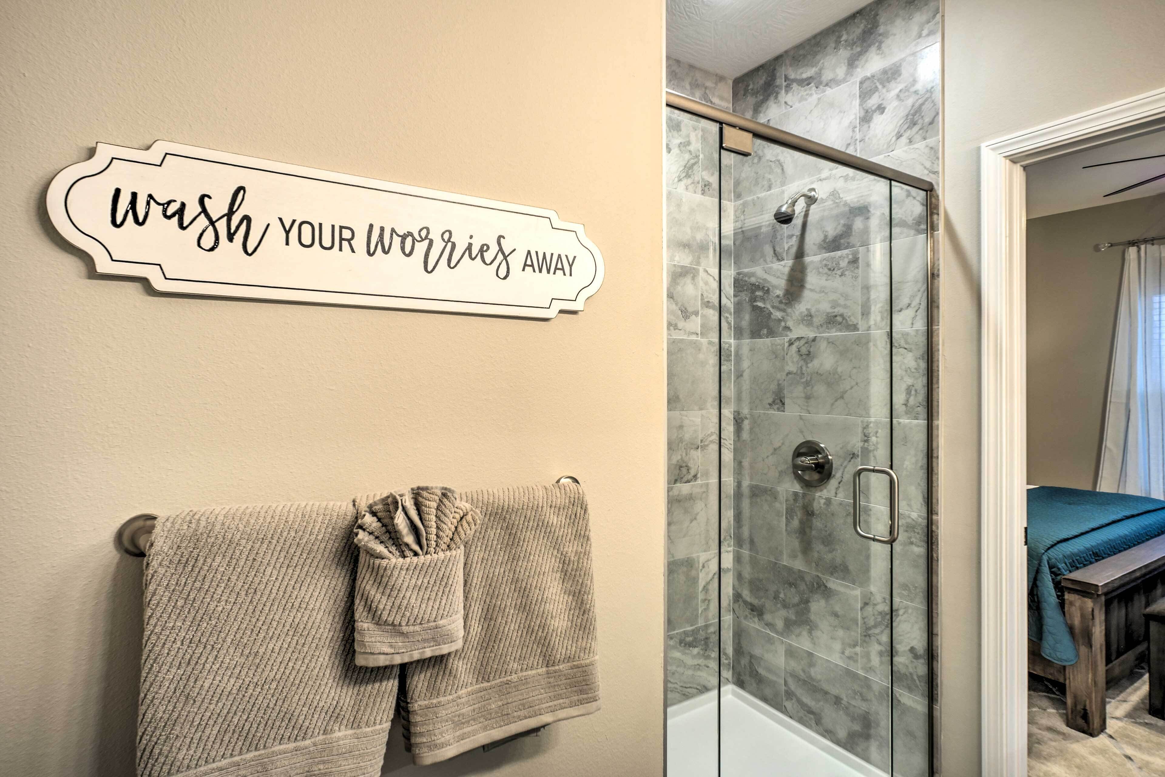 A bathroom with a glass shower enclosure, a towel rack with two towels, and a sign that reads "wash your worries away".