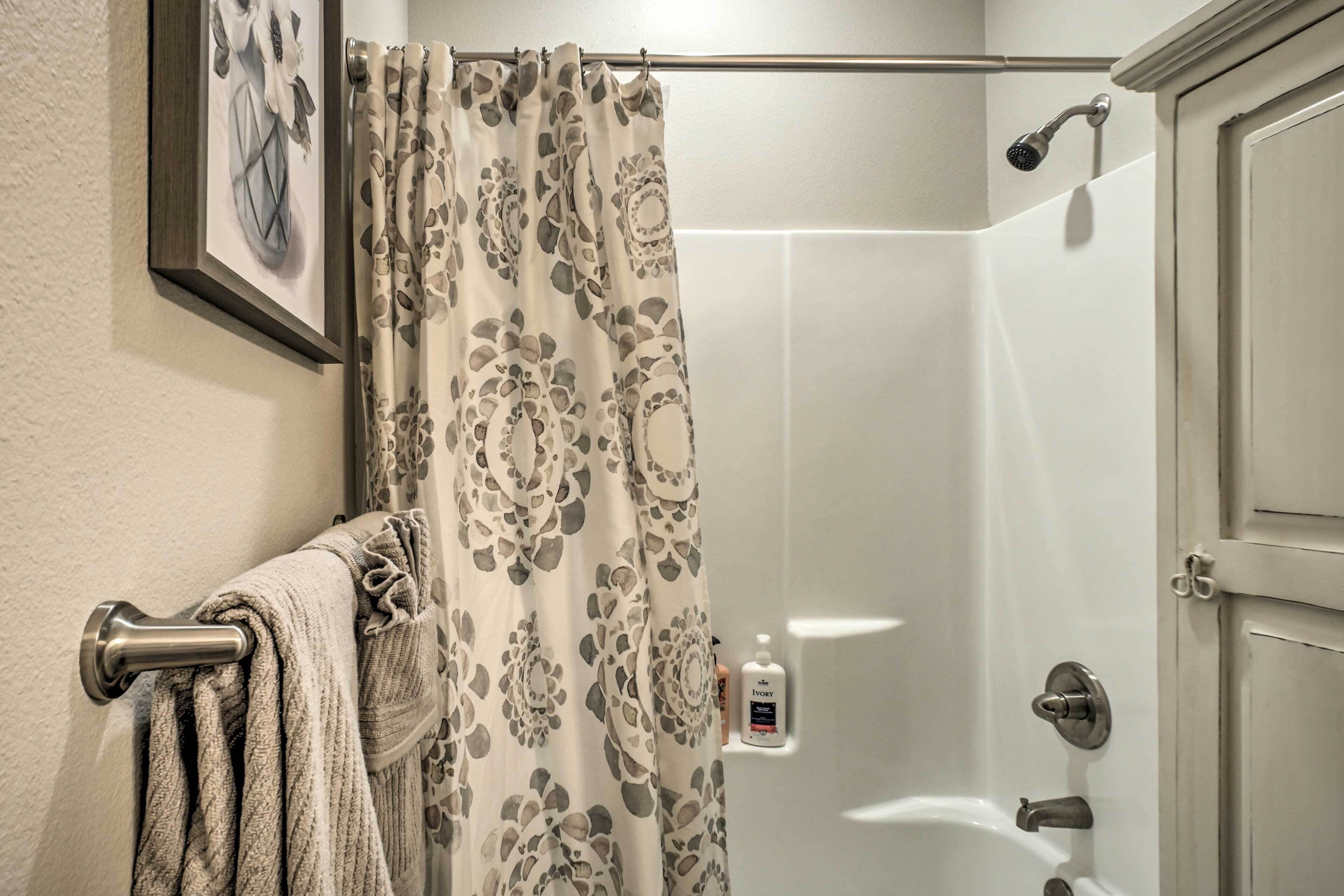 A bathroom with a shower curtain, a towel rack with towels, a showerhead, and a bottle of Ivory soap.